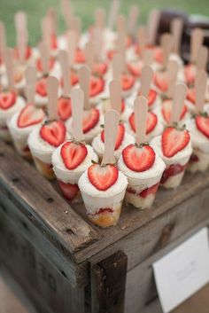 cupcakes with strawberries are arranged on a wooden box and placed on sticks