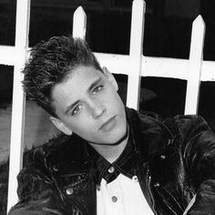 a young man leaning against a white fence