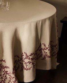 a table with two glasses on it and a white tablecloth that has red vines on it