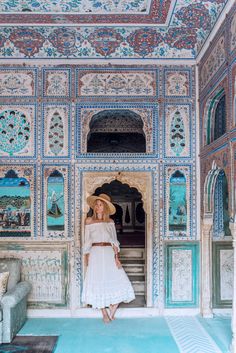 a woman in a white dress and straw hat standing in an ornately decorated room