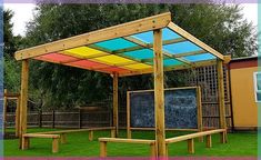 a wooden bench sitting under a colorful glass covered shelter on top of a lush green field