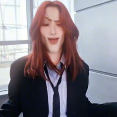 a woman with long red hair wearing a suit and tie in front of a window