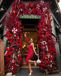 a woman standing in front of a store decorated with red flowers and candy canes