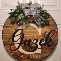 a wooden sign hanging on the side of a door with greenery and ribbon around it