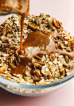 a glass bowl filled with granola, nuts and caramel syrup being poured into it