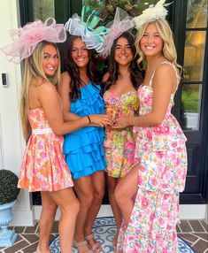 four women in dresses and hats posing for a photo on the front steps of a house