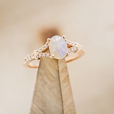 a white opal and diamond ring on top of a wooden stand