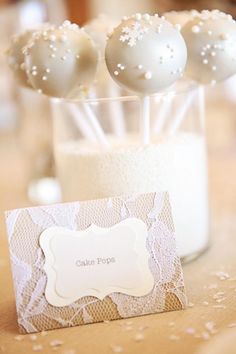 some white balls are in a glass vase on a table with a card and place cards