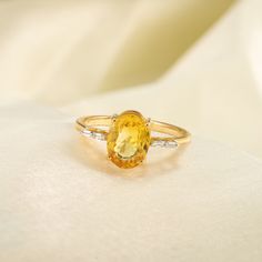 an oval shaped yellow sapphire and diamond ring on a white cloth with the background visible