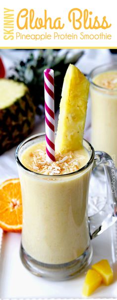 two glasses filled with smoothie next to sliced oranges and pineapple on the side