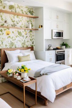 a white bed sitting in a bedroom next to a wooden table with flowers on it