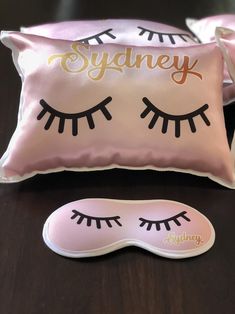 two pillows with eyelashes on them next to a sleeping mask and eyeliner sticker