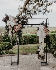 an arch decorated with flowers and greenery for a wedding ceremony in the middle of a field