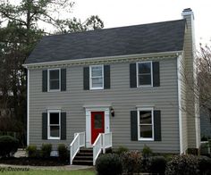 a gray house with red door and steps leading up to the front door is shown