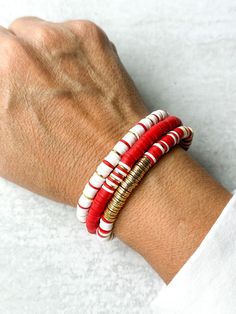 a person's arm wearing three bracelets with red, white and gold beads