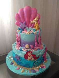 a three tiered cake decorated with mermaids and seashells