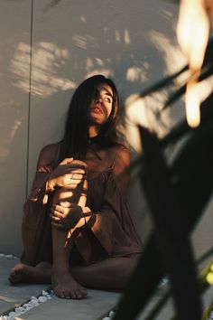 a woman sitting on the ground next to a plant