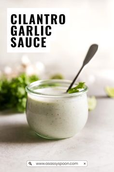 a glass jar filled with white sauce and garnished with cilantro on the side