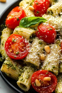 pasta with pesto, tomatoes and pine nuts in a black bowl on a white table