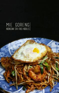 a blue and white plate topped with noodles and an egg on top of fried meat