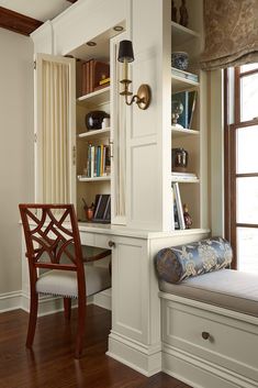 a room with a window seat and bookshelf next to a desk in the corner