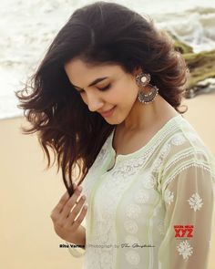 a woman standing on top of a sandy beach next to the ocean with her hair blowing in the wind