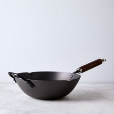 an empty frying pan with a wooden handle on a marble countertop next to a white wall