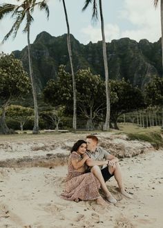 a man and woman are sitting on the sand under palm trees in front of mountains