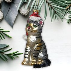 a cat ornament hanging from a christmas tree with pine branches in the background