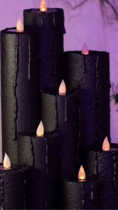 several black candles are lit in front of a purple background