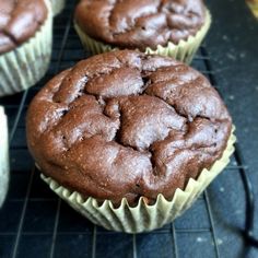 three chocolate muffins cooling on a rack with other muffins in the background