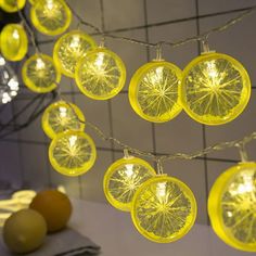 some yellow lights are hanging from a wire near oranges and other fruit on the table