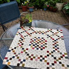 a table with a quilt on top of it next to some chairs and potted plants