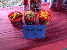 a table topped with red buckets filled with different types of food next to cans of soda