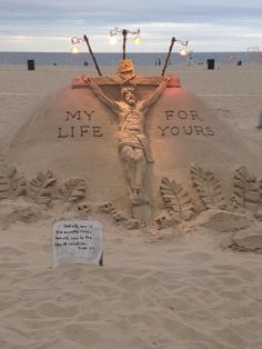 a sand sculpture on the beach that says, my life for yours with a crucifix