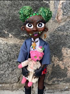 a doll with green hair holding a pink teddy bear in front of a stone wall