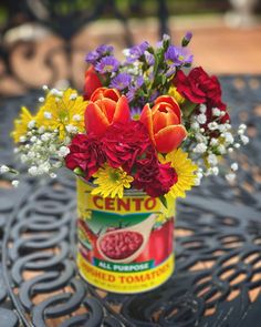 a can filled with lots of flowers sitting on top of a metal table next to a bench