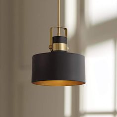 a black and gold pendant light hanging from a ceiling in a room with sunlight coming through the window