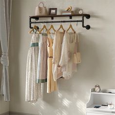 a rack with clothes hanging on it next to a white dresser and window sill