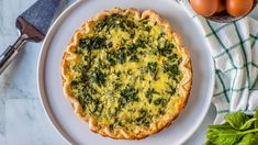 a quiche with spinach and eggs on a white plate next to some greens