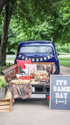 the back of a blue truck filled with food next to a sign that says it's game day