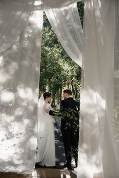 the bride and groom are standing under white drapes at their wedding ceremony in the park