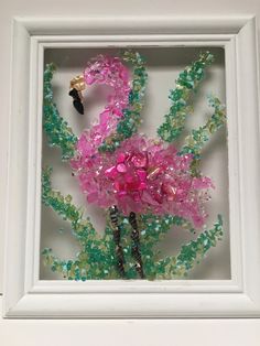 a white frame holding a pink and green flower in it's center with beads