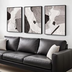 a living room with black leather couches and two paintings on the wall above them