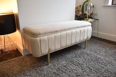 a white bench sitting on top of a carpeted floor next to a lamp and window