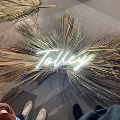 the word toiley written in neon lights on top of some grass and someone's feet