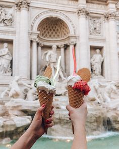 two people holding ice cream cones in front of a fountain