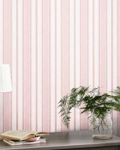 a desk with a lamp, book and potted plant on it next to a pink striped wallpaper