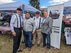 three men standing next to each other in front of a tent at an outdoor event