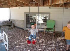 two young boys sitting on swings in front of a house with rocks and gravel covering the ground